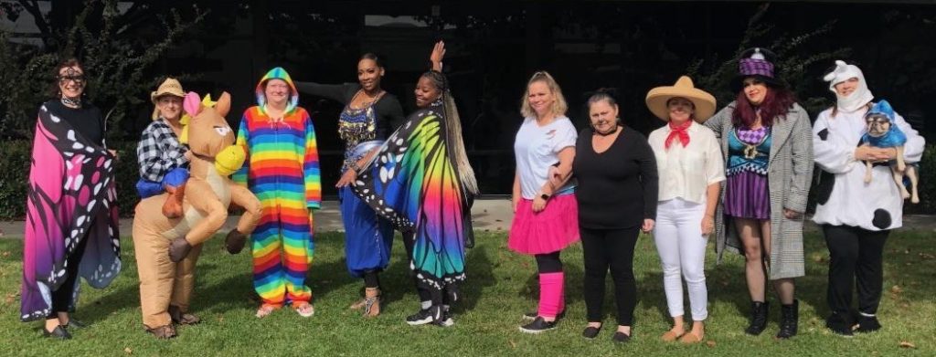 A bunch of ladies standing in front of office celebrating halloween in costumes